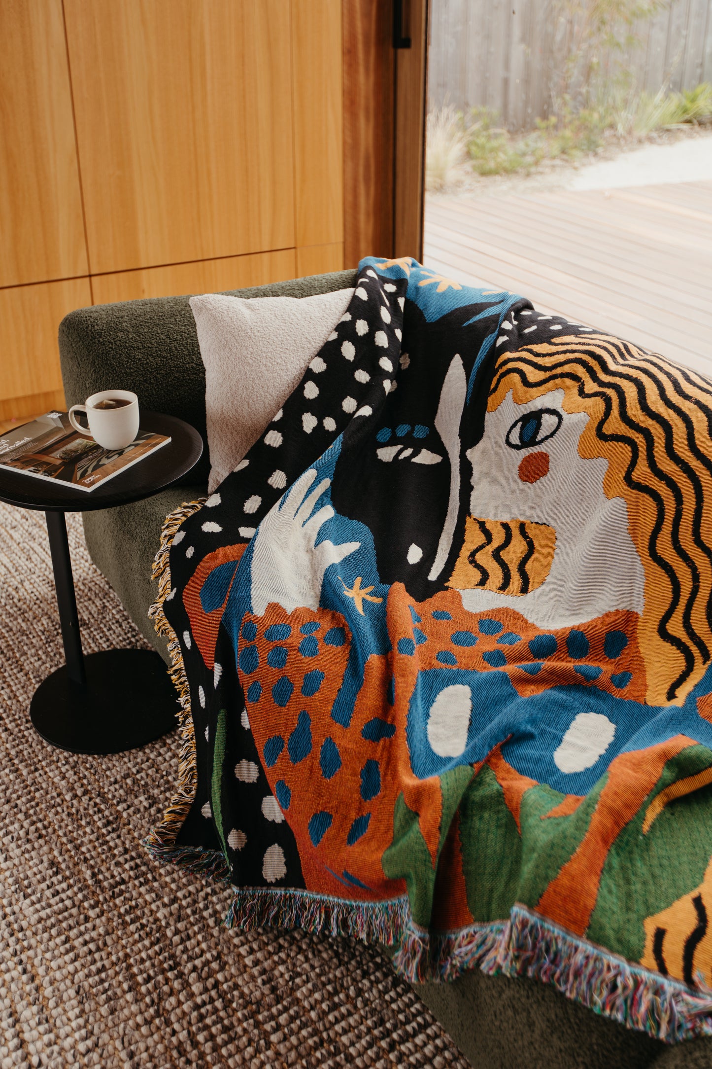 Alma woven blanket by Enikő Katalin Eged draped over armchair, showcasing expressive illustration and rich jacquard texture