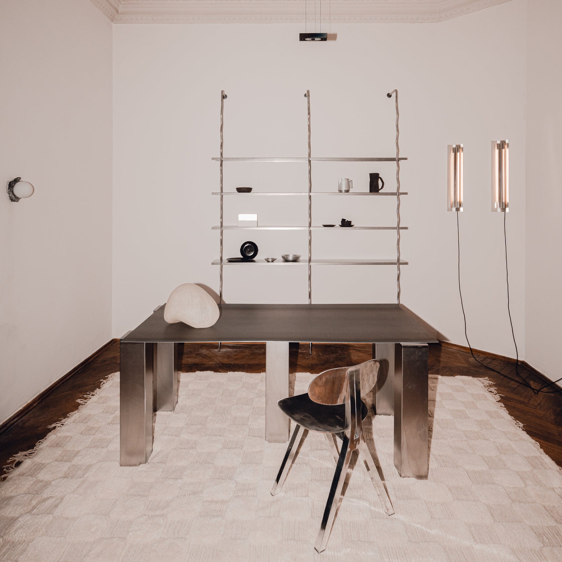 WAVE floor-to-ceiling steel shelving unit in a minimalist interior with dark table and chair, by The Good Living & Co.