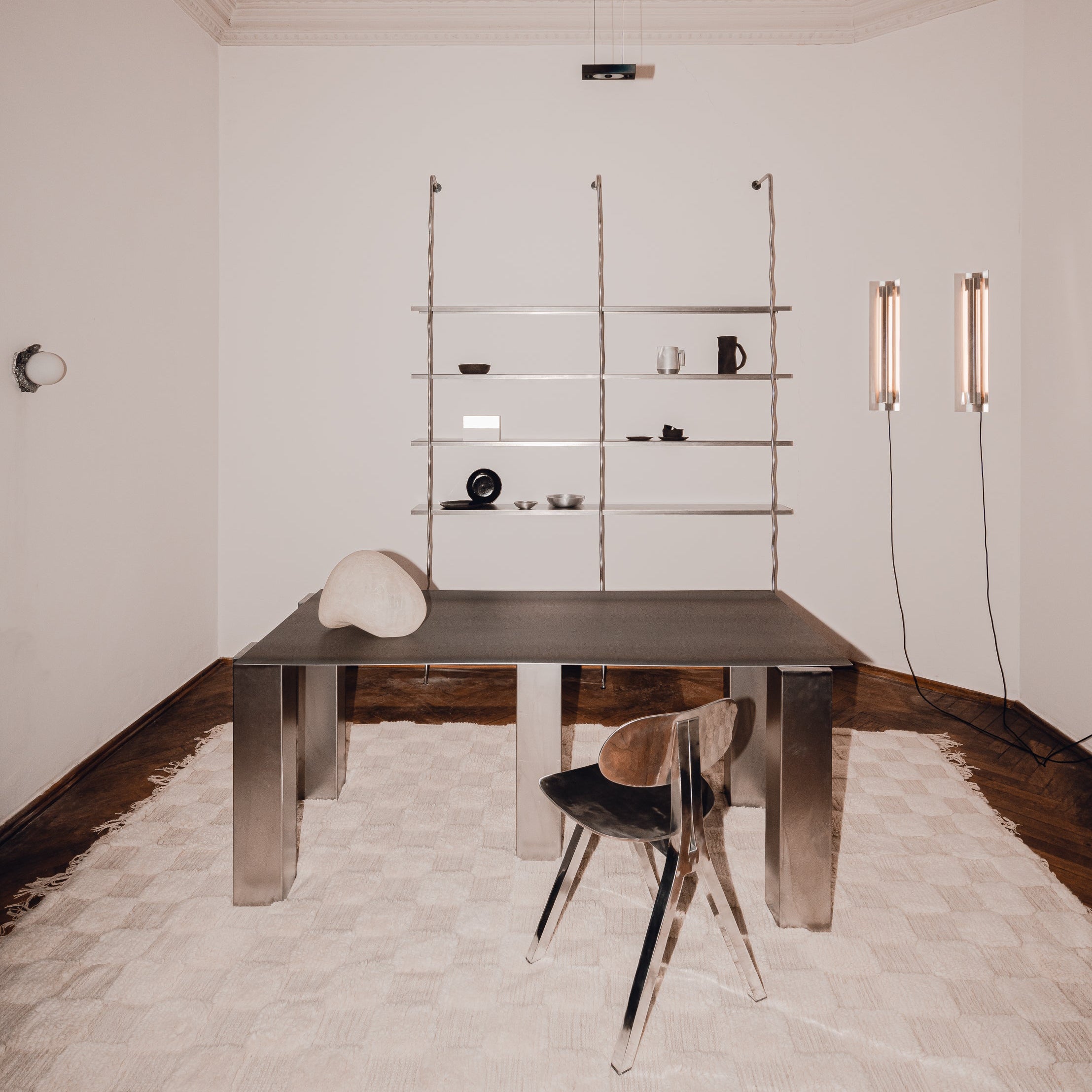 WAVE floor-to-ceiling steel shelving unit in a minimalist interior with dark table and chair, by The Good Living & Co.