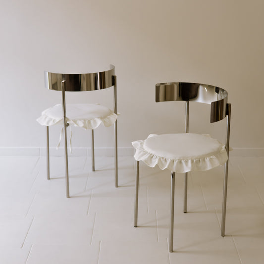 Two MEADOW chairs with polished stainless steel frames and white ruffled seat cushions, by The Good Living & Co.