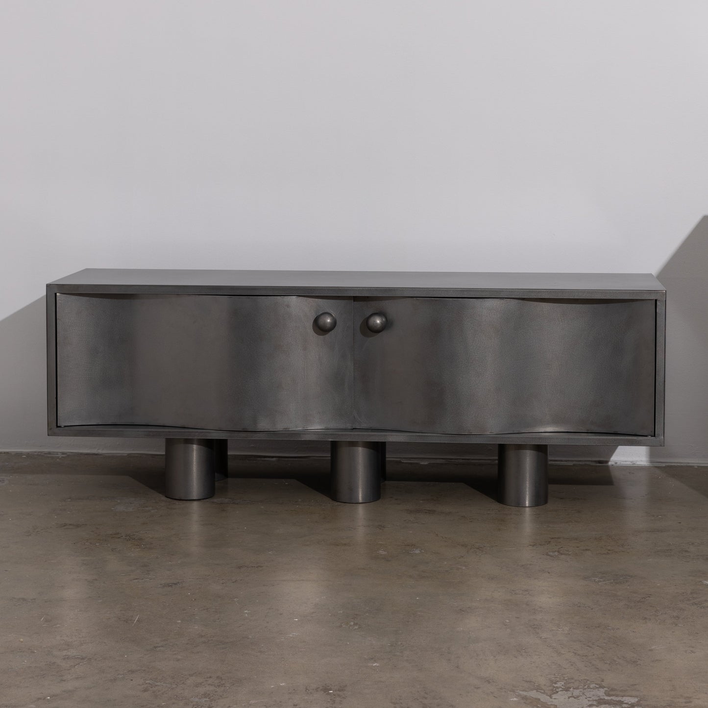 MOTION commode in brushed  steel with curved front doors, round knobs and cylindrical legs, by The Good Living & Co.