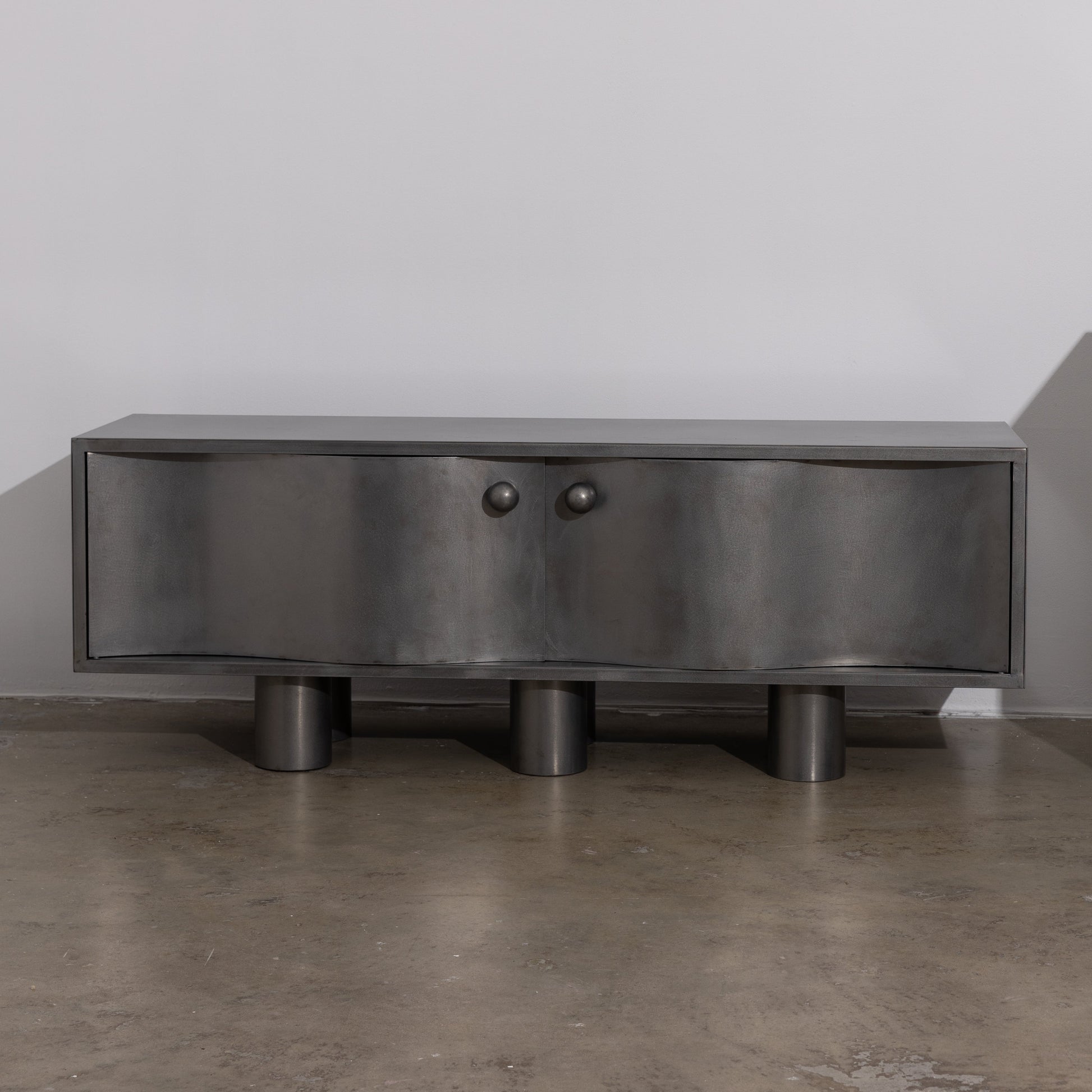 MOTION commode in brushed  steel with curved front doors, round knobs and cylindrical legs, by The Good Living & Co.