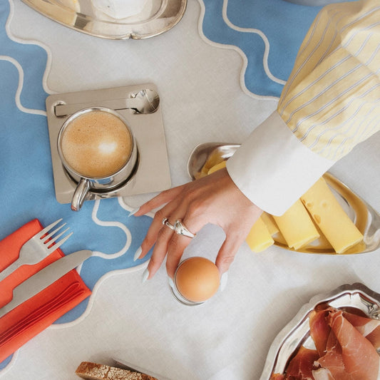 Breakfast setup with coffee, bread, and prosciutto on a patterned tablecloth.