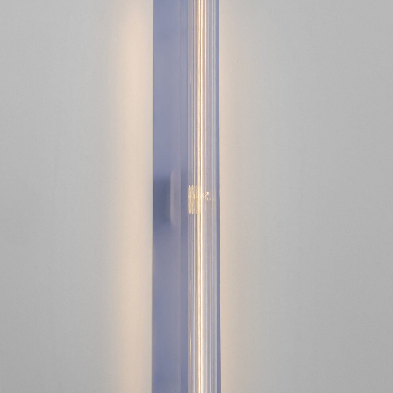 A modern vertical wall sconce with a translucent lavender-blue rectangular housing and a glowing warm white tube light inside, mounted on a plain light gray wall.