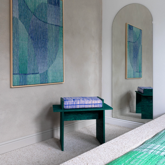 Room interior with abstract art on wall and mirror, green bench, and bed. Custom made stool by Emma Terweduwe