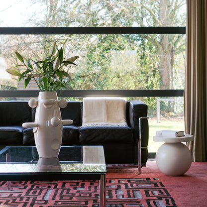 Rocket vase sculpture by Malwina Konopacka — white ceramic piece with pretzel and ball motifs, placed on a table by a window overlooking the forest.