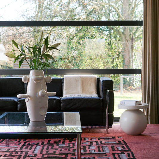 Rocket vase sculpture by Malwina Konopacka — white ceramic piece with pretzel and ball motifs, placed on a table by a window overlooking the forest.