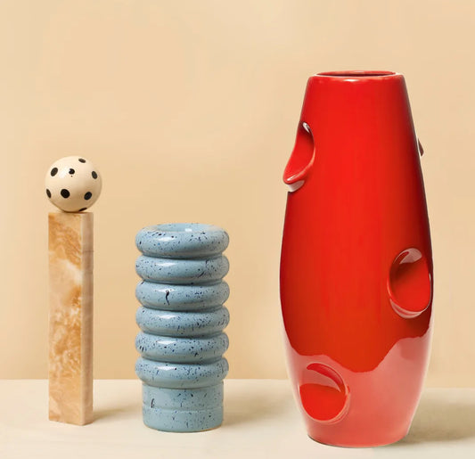 Red oval-shaped vase by Malwina Konopacka featuring geometric recesses, styled with a blue sphere and beige cylinder on a neutral background — contemporary Polish ceramic design.
