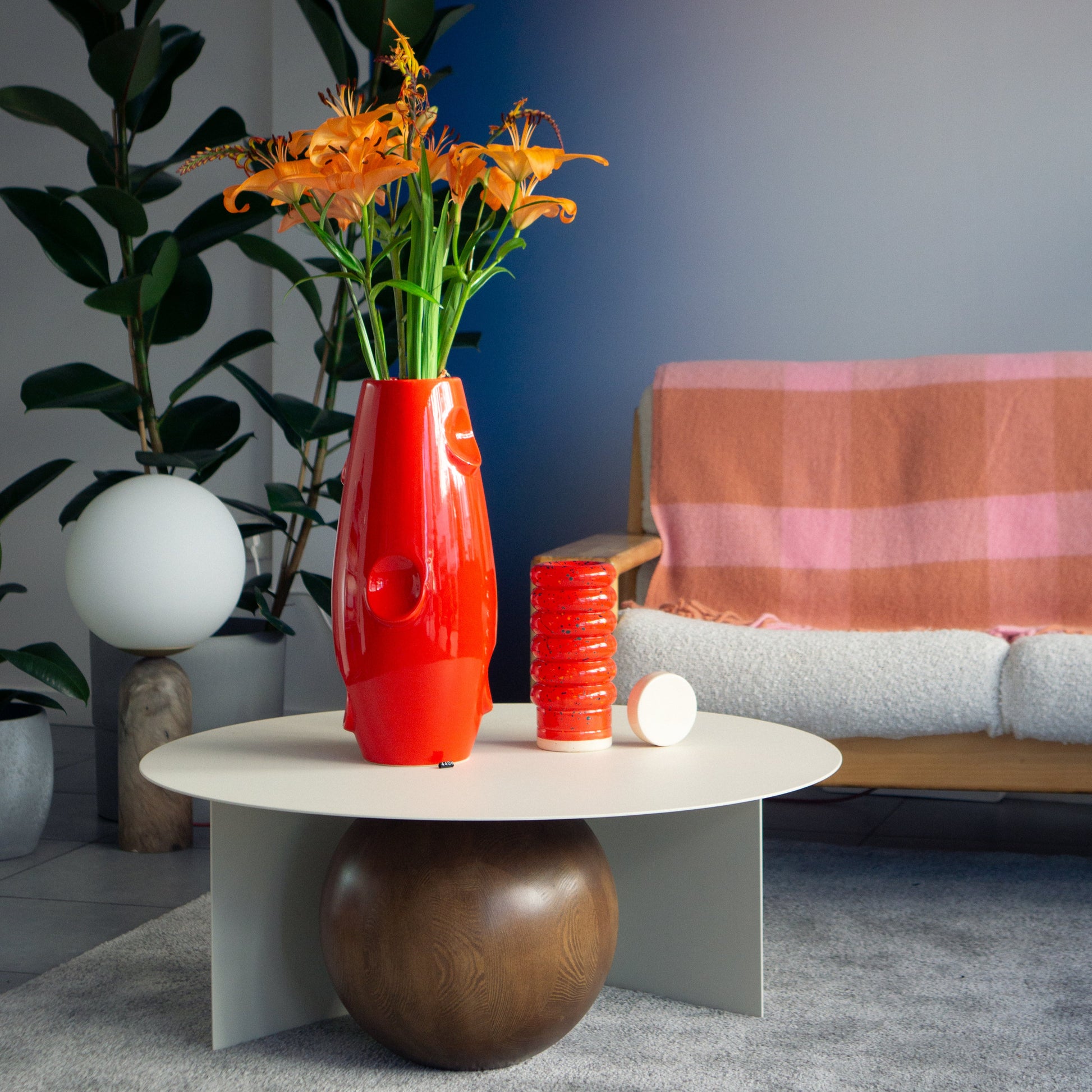 Unique red NANA vase by Malwina Konopacka with dark blue and geen details and orange lilies, styled on a round white table in a modern living room — contemporary design available at RUIMTE.