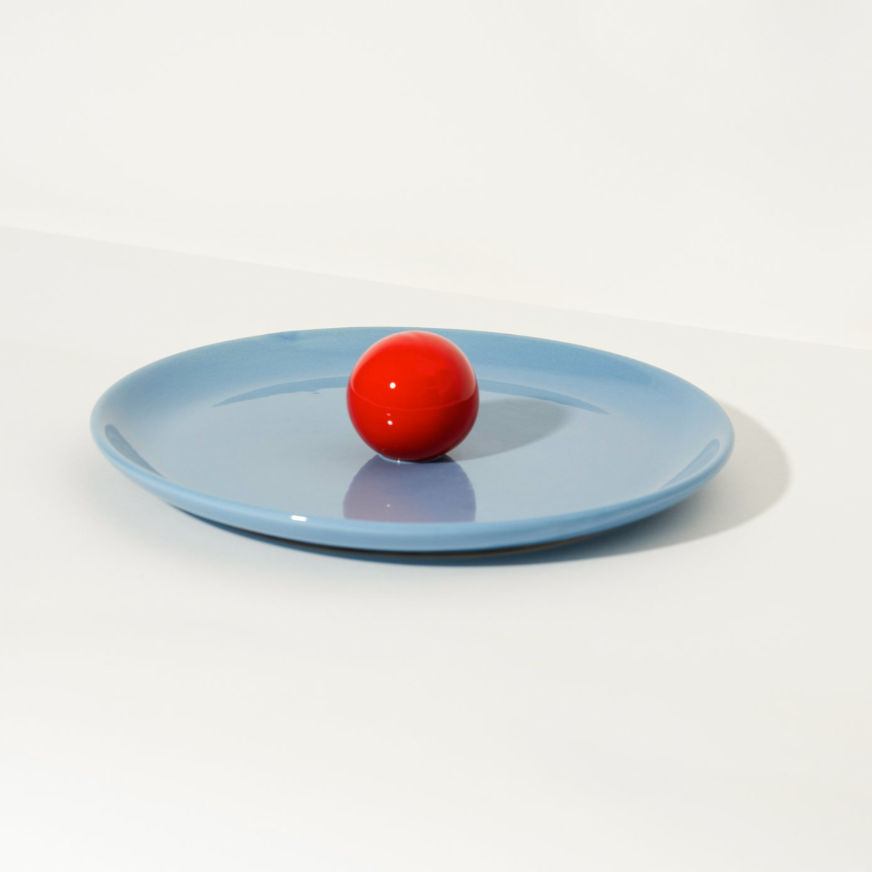 Blue ceramic fruit platter by Malwina Konopacka with a ball-shaped handle, styled on a white background.