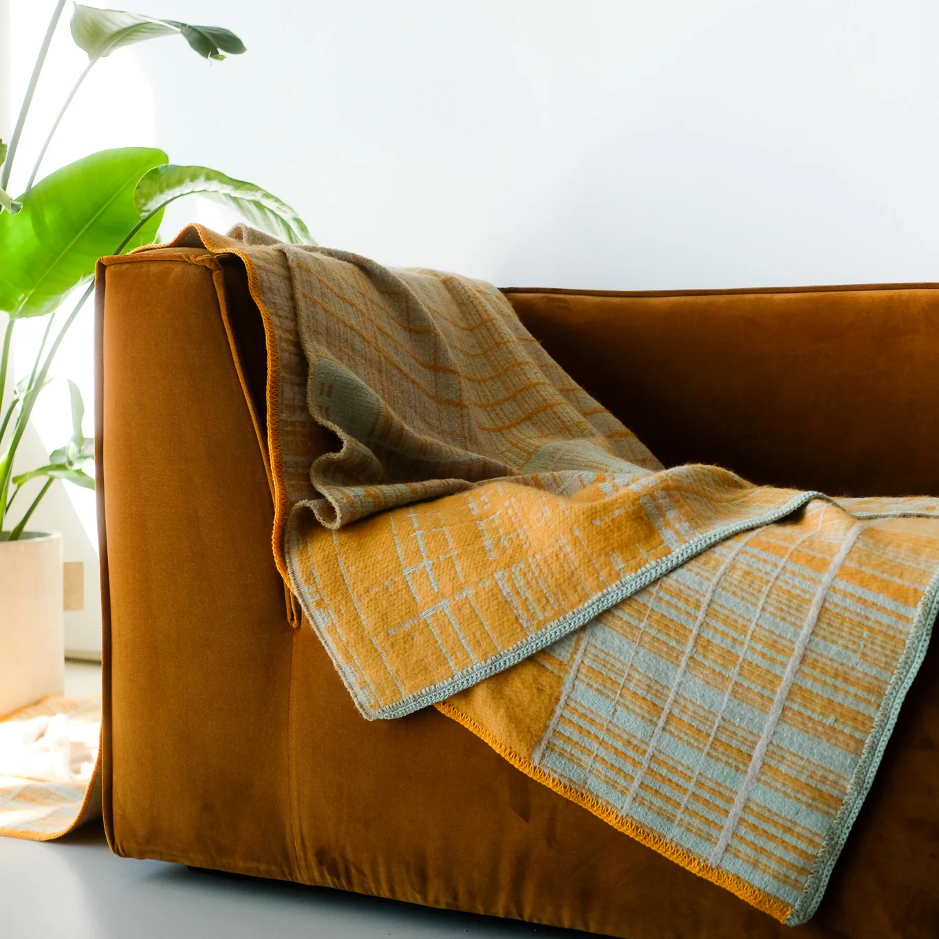 Jacquard-woven plaid blanket by Emma Terweduwe draped over a mustard velvet sofa