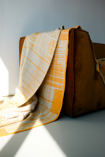Jacquard-woven plaid blanket by Emma Terweduwe styled on armchair in soft daylight
