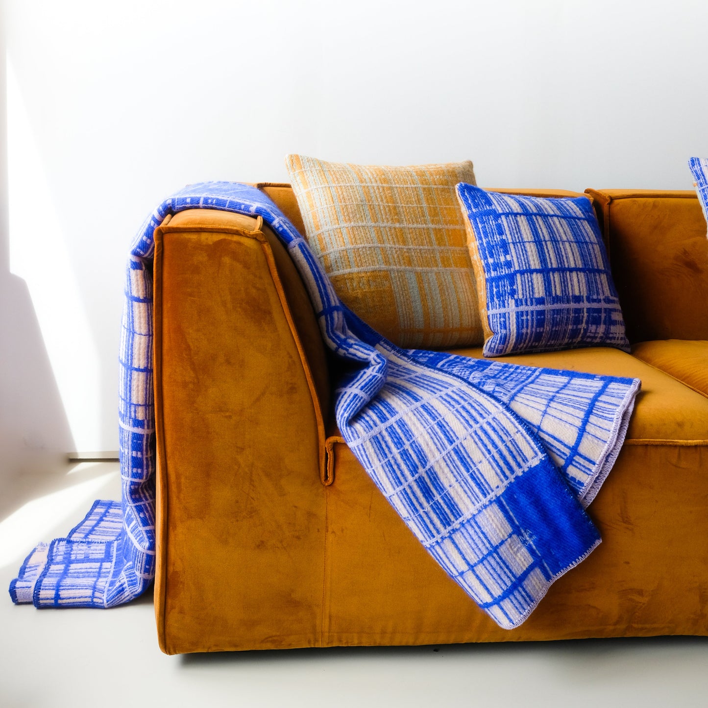 Jacquard-woven blanket by Emma Terweduwe draped over a mustard velvet sofa