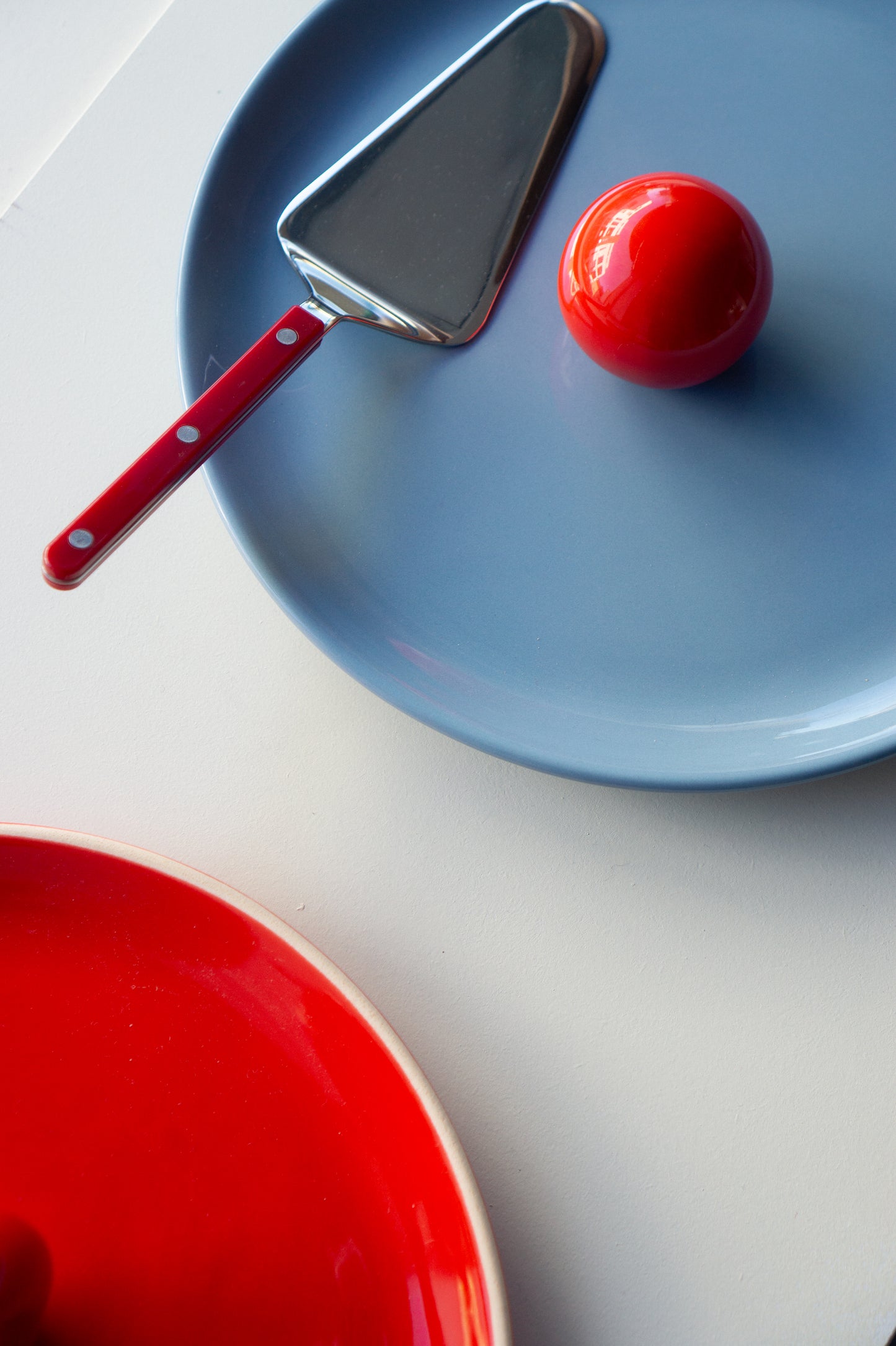 Blue ceramic fruit platter by Malwina Konopacka with a ball-shaped handle, styled on a white background ans Sabre Paris cutlery, part of Ruimte concept collection.