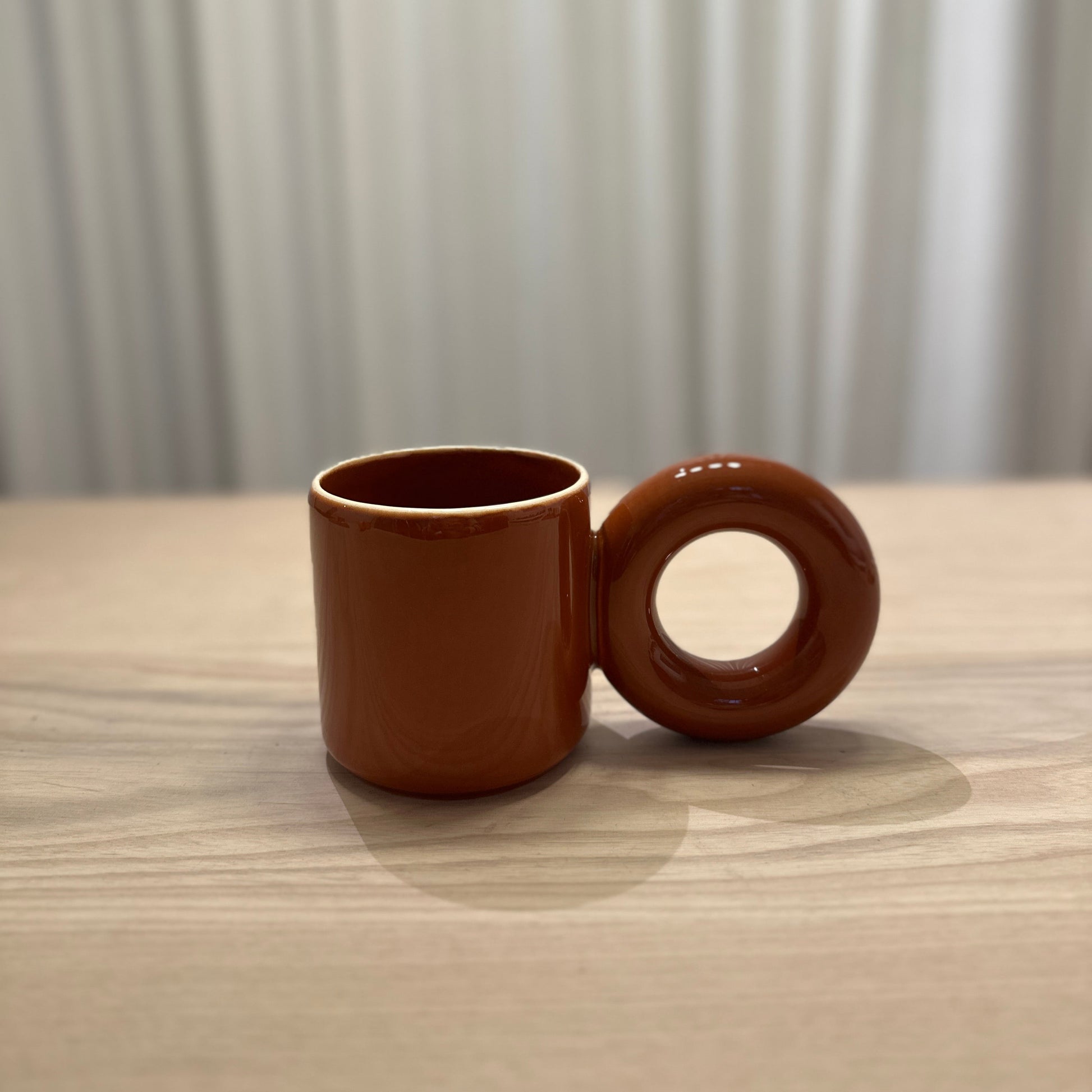 Brown mug by Malwina Konopacka featuring the sculptural round handle and handcrafted ceramic finish from the RUIMTE curated collection.