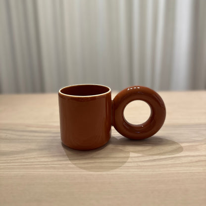 Brown mug by Malwina Konopacka featuring the sculptural round handle and handcrafted ceramic finish from the RUIMTE curated collection.