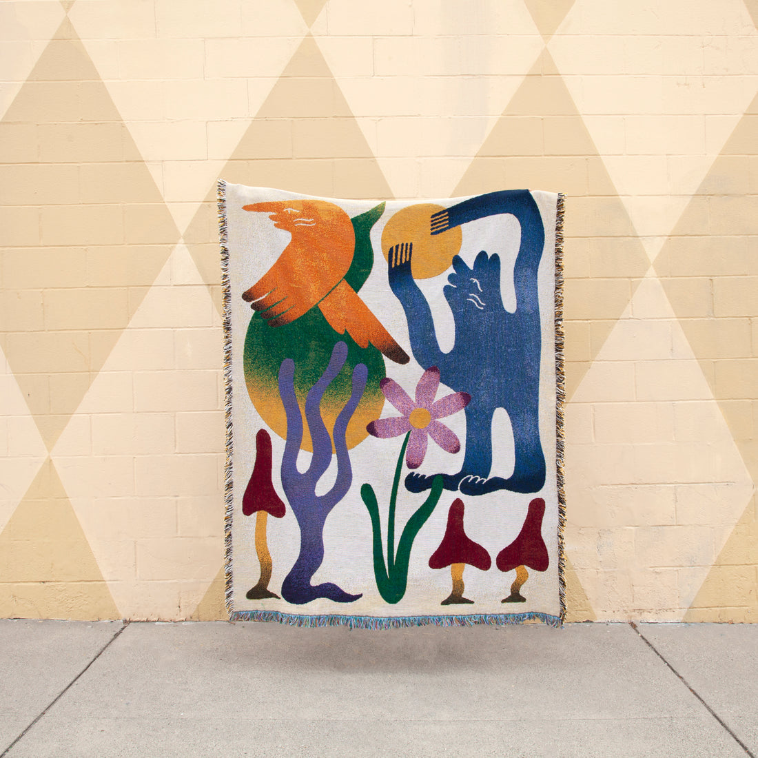 Dumont woven throw blanket by Roisin O’Donnell hanging as textile wall art against a patterned wall